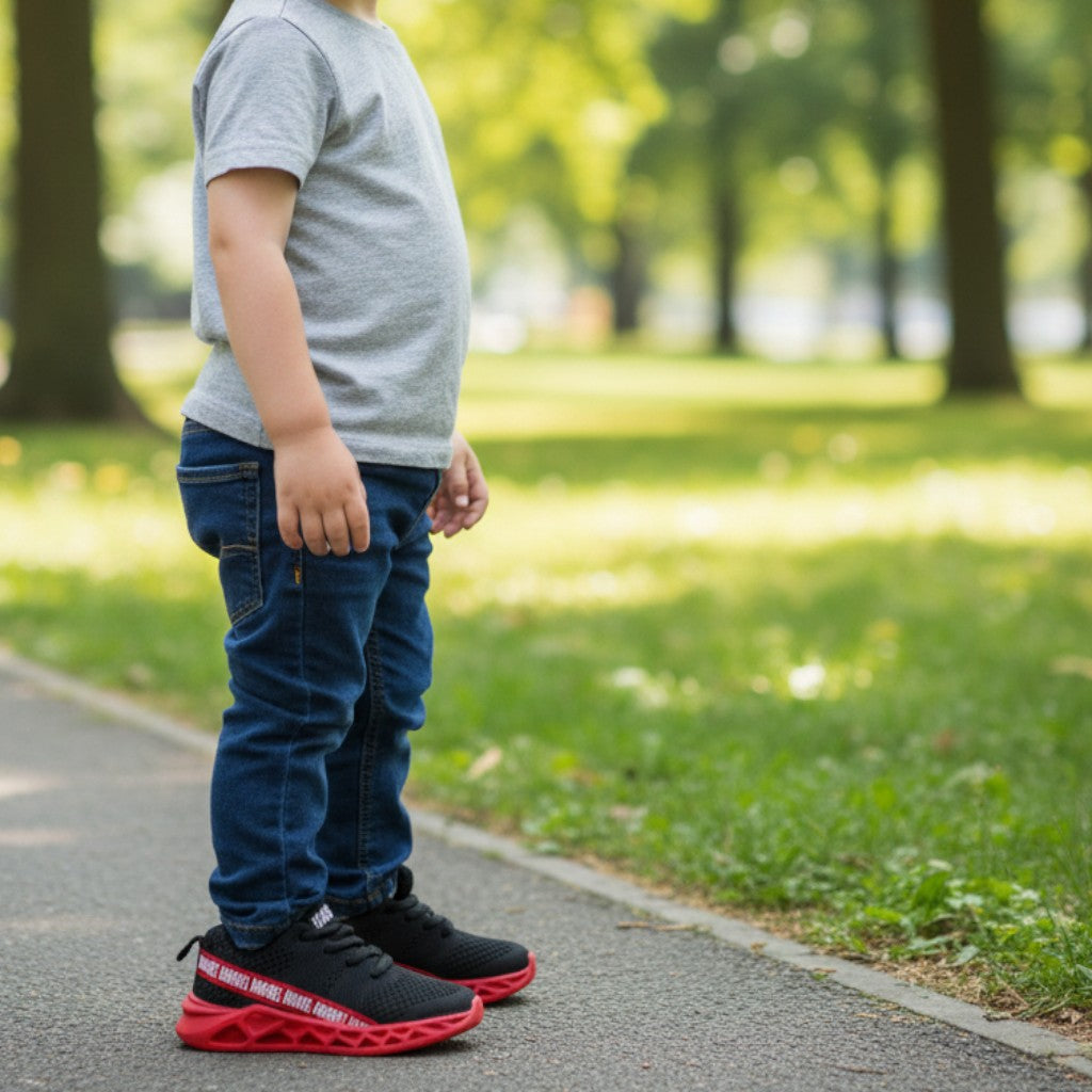 Enfant portant baskets Marvel rouges et noires, jeans et t-shirt gris, debout dehors dans un parc